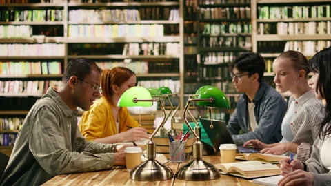 Classmates and tutor in study group working with open books at library desk Stock Footage 336358161