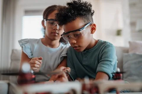 Classmates assembling robotic kit, working with circuit board at home. Stock Photos