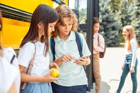Classmates going to school by bus boy showing girl game on smartphone smiling Stock Photos