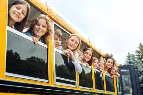 Classmates going to school by bus leaning out of the window smiling happy Foto stock