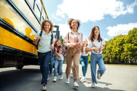 Classmates running from school bus back home looking forward smiling happy Stock Photos