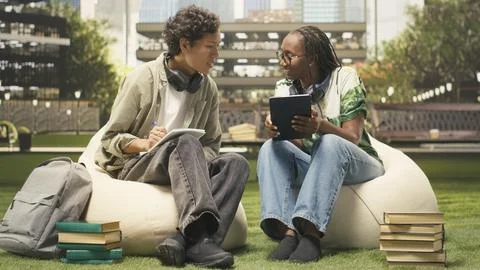 Classmates sharing ideas with open laptop seated on campus beanbags Stock Photos