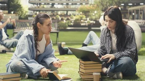 Classmates in study session sitting on grass with laptop placed on stacked books Stock Photos