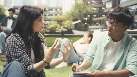 Classmates in study session sitting on grass with laptop placed on stacked books Stock Photos