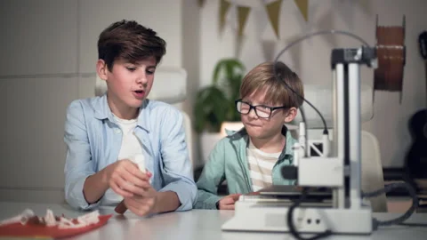 In classroom on lesson older boy explaining to young boy how 3D printer work Stock Footage 335373207