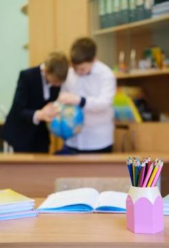 Classroom scene featuring students engaged with a globe while a colorful pencil Photos