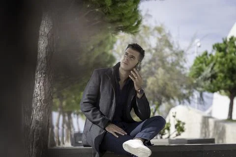 Classy freelance architect sitting alone on a bench outdoor and talking on th Foto stock