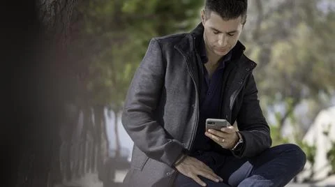 Classy freelance architect sitting alone on a bench outdoor and talking on th Stock Photos