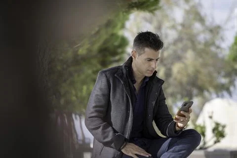 Classy freelance architect sitting alone on a bench outdoor and talking on th Stock Photos