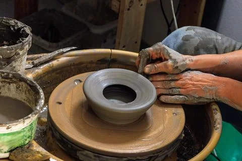 Clay covered hands shaping and trimming a wet clay vessel on a spinning pot.. Stock Photos