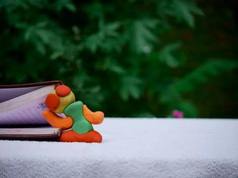 A clay doll putting head between the book pages at white surface on green blu Stock Photos
