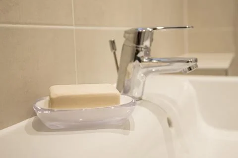 Clean bar soap rests in a clear dish beside a sleek faucet Stock Photos