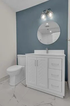 Clean bathroom with a white vanity, round mirror, and modern light fixture. Фото