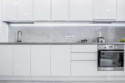 A clean, bright kitchen featuring all-white cabinets and a modern design Stock Photos