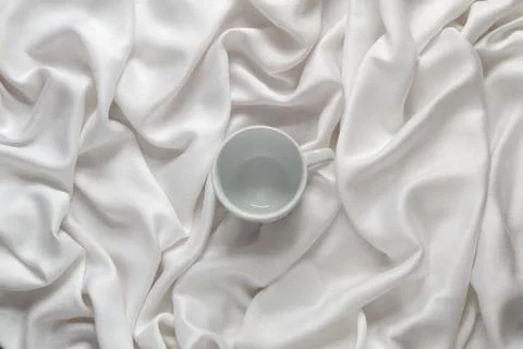 Clean ceramic empty coffee cup on the silk white fabric. Top view Stock Photos