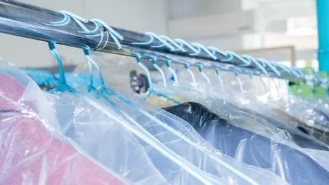 Clean clothes protected with plastic hanging on a rack in a laundry Stock Photos