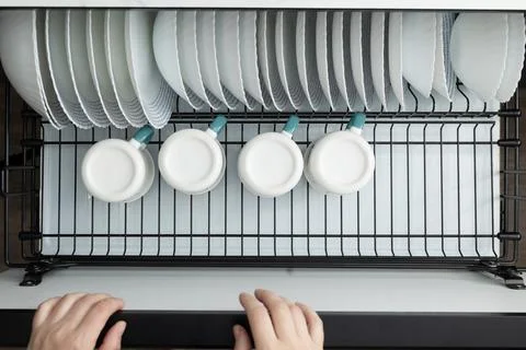 Clean Dishes in a Drying Rack Being Organized in a Modern Kitchen Stock Photos