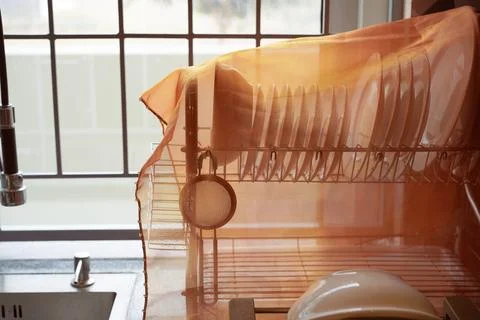 Clean dishes on a drying rack covered with a transparent cloth for protection. Stock Photos