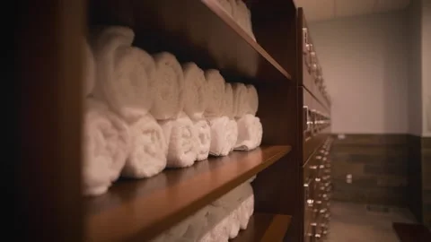 Clean, empty gym locker room with rolled white towels on shelves next to Stock Footage 131610656