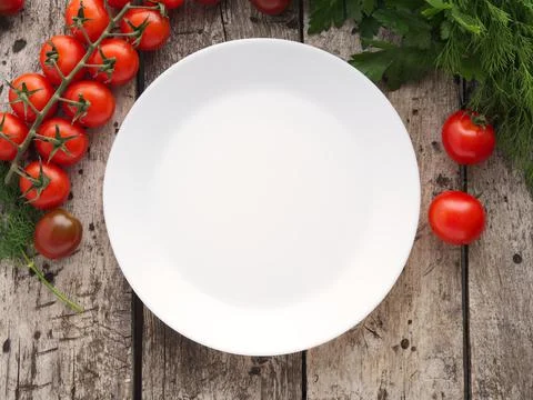 Clean empty white plate and vegetables, tomato, parsley on old rustic wooden Stock Photos