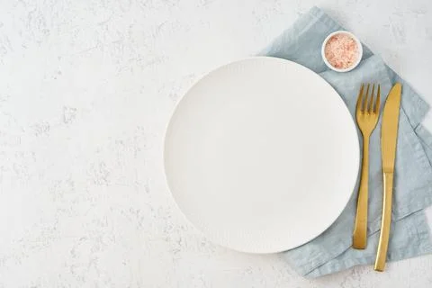 Clean empty white plate, fork and knife on white stone table, copy space, mock Stock Photos
