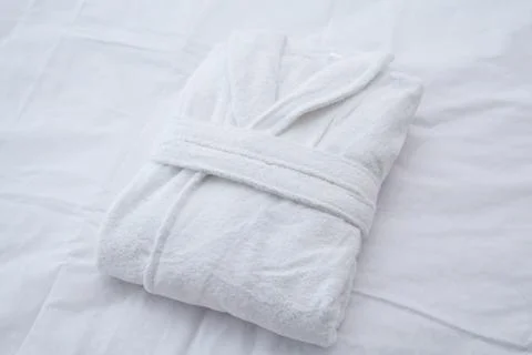 Clean folded bathrobe on white bed. Stock Photos