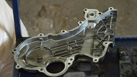 A clean metallic timing chain cover component lies disassembled on a blue tra Stock Footage 345109126