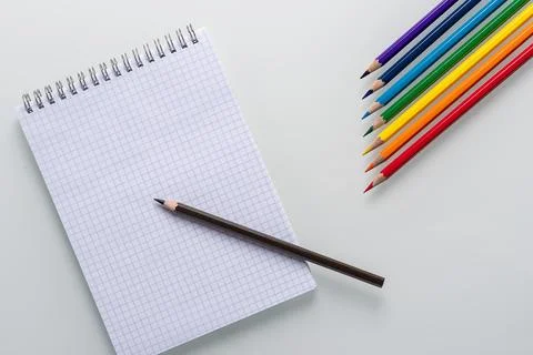 Clean notepad in a cage with a pencil lying on it and color pencils in the form Stock Photos