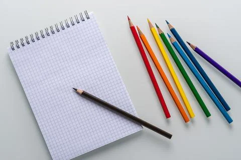 Clean notepad in a cage with a pencil lying on it and rainbow color pencils on a Stock Photos