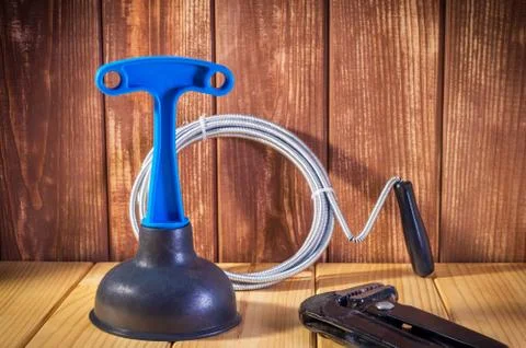 Clean plastic plunger with blue handle, pipe wrench and cable on wooden Stock Photos