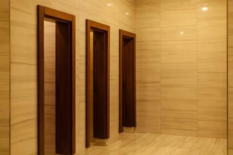 A clean restroom area features three elegant wooden doors set into sleek marb 스톡 사진