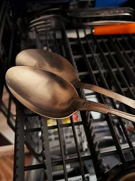 Clean silver spoons inside a dishwasher rack after washing cycle. Fotos Stock