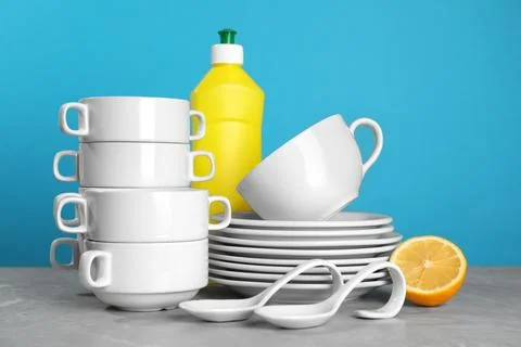 Clean tableware, dish detergent and lemon on grey table against light blue .. Stock Photos
