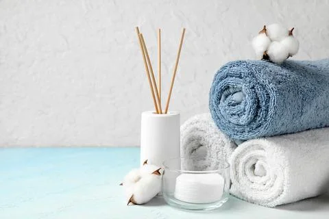 Clean towels, reed diffuser and cotton pads on table against light wall Stock Photos