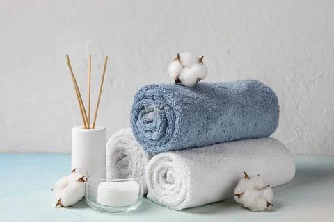 Clean towels, reed diffuser and cotton pads on table against light wall Stock Photos