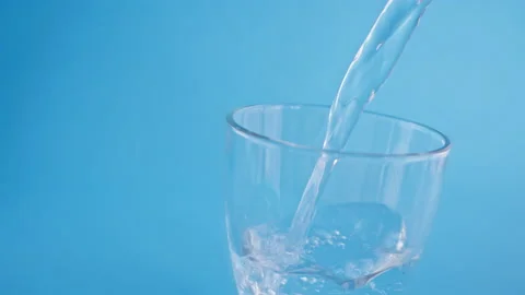 Clean, transparent drinking water is slowly poured into a glass glass on a blue Stock Footage 235623635