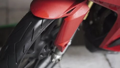 Clean water from a hose pours onto the motorcycle wheel, washing away the Stock Footage 237303353