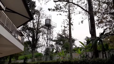 Clean Water Tower Under Cloudy Gray Sky Near Trees And Residential Buildings Stock Footage 317933223