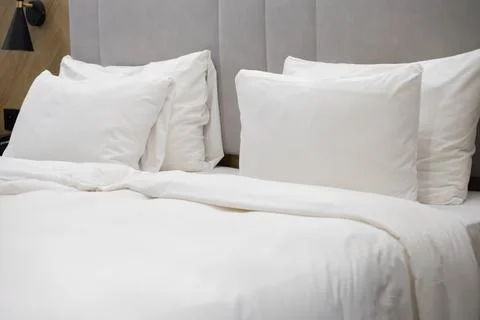 Clean white bedding on a comfortable hotel bed with soft pillows against a Stock Photos