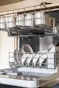 Clean white dishes stacked inside an open dishwasher machine in a modern ki.. Stock Photos