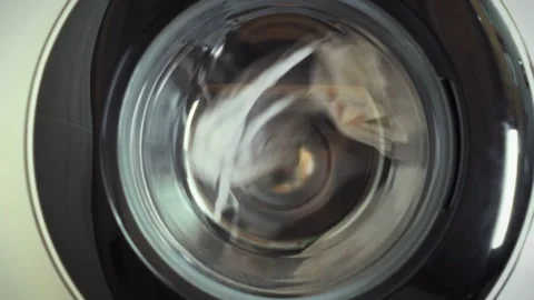 Clean white laundry is visible through the transparent window of a front-loa Stock Footage 331348543