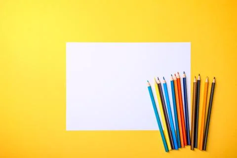 A clean white sheet and colored pencils for drawing on a yellow background wi Stock Photos