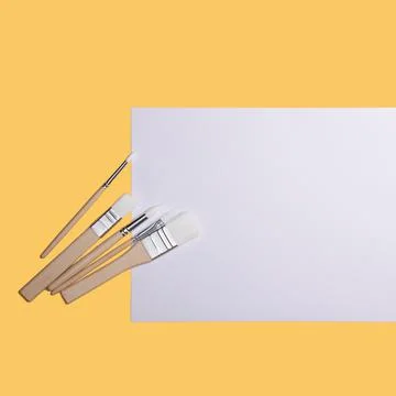 A clean white sheet and paint brushes on a yellow background with a place to  Stock Photos