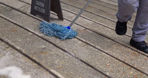 Cleaner mopping stone stairs with blue mop near wet floor sign Stock Footage 344461757