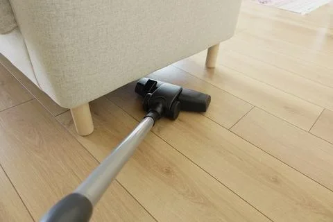 Cleaner uses vacuum under couch in living room during the day Stock Photos