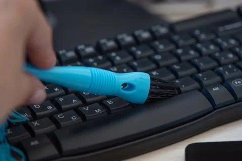 Cleaning and caring computer keyboard with a blue brush from dust. Stock Photos