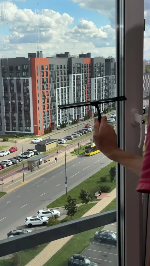 Cleaning apartment balcony windows with a rubber glass squeegee device. Wor.. Stock Footage 345526801