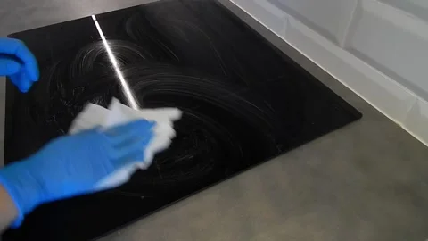 Cleaning a black induction cooker with a white cloth in blue gloves Stock Footage 309000728