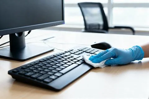 Cleaning a computer keyboard with a sanitizing wipe in an office setting 스톡 사진