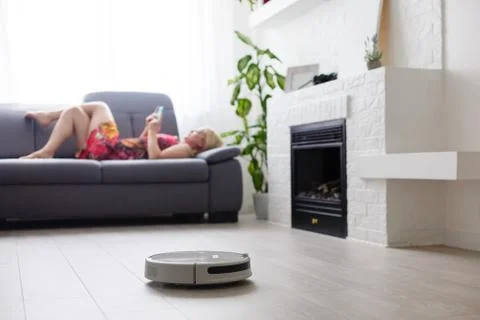 Cleaning concept - automatic robotic hoover clean the room while woman relaxi Foto stock
